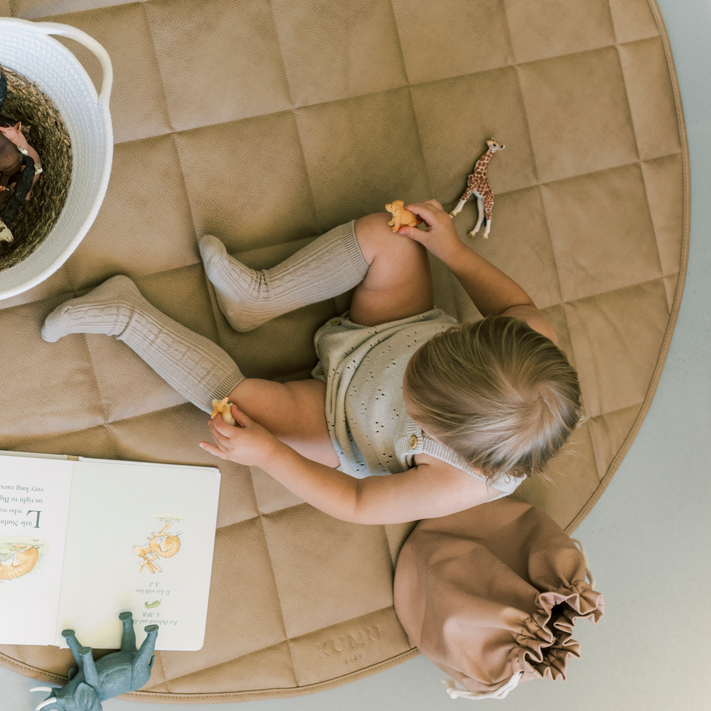 Overhead photo of a toddler girl sitting on a vegan leather play mat while playing with toys.